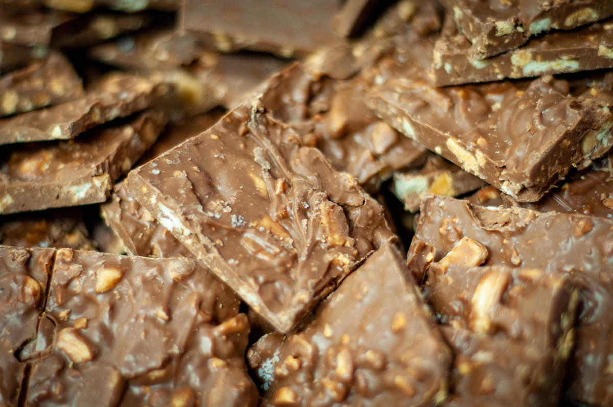 Bulk Salty Monkey Milk Chocolate Bark pieces stacked closely, peanuts and banana chips visible throughout the milk chocolate. Main image