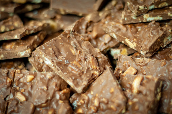 Bulk Salty Monkey Milk Chocolate Bark pieces stacked closely, peanuts and banana chips visible throughout the milk chocolate.