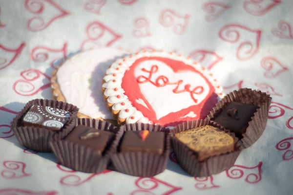 Valentine's Seasonal Variety — heart-shaped iced cookies (one with 'Love' lettering) and chocolate bonbons on a heart-patterned background.
