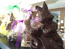 Dark chocolate Easter bunny-on-turtle sculpture in the foreground with cellophane-wrapped Easter chocolates and ribbons behind.