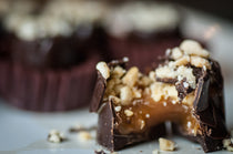 Group of Peanut Caramel Cups in burgundy paper liners, each topped with crushed peanuts on chocolate.