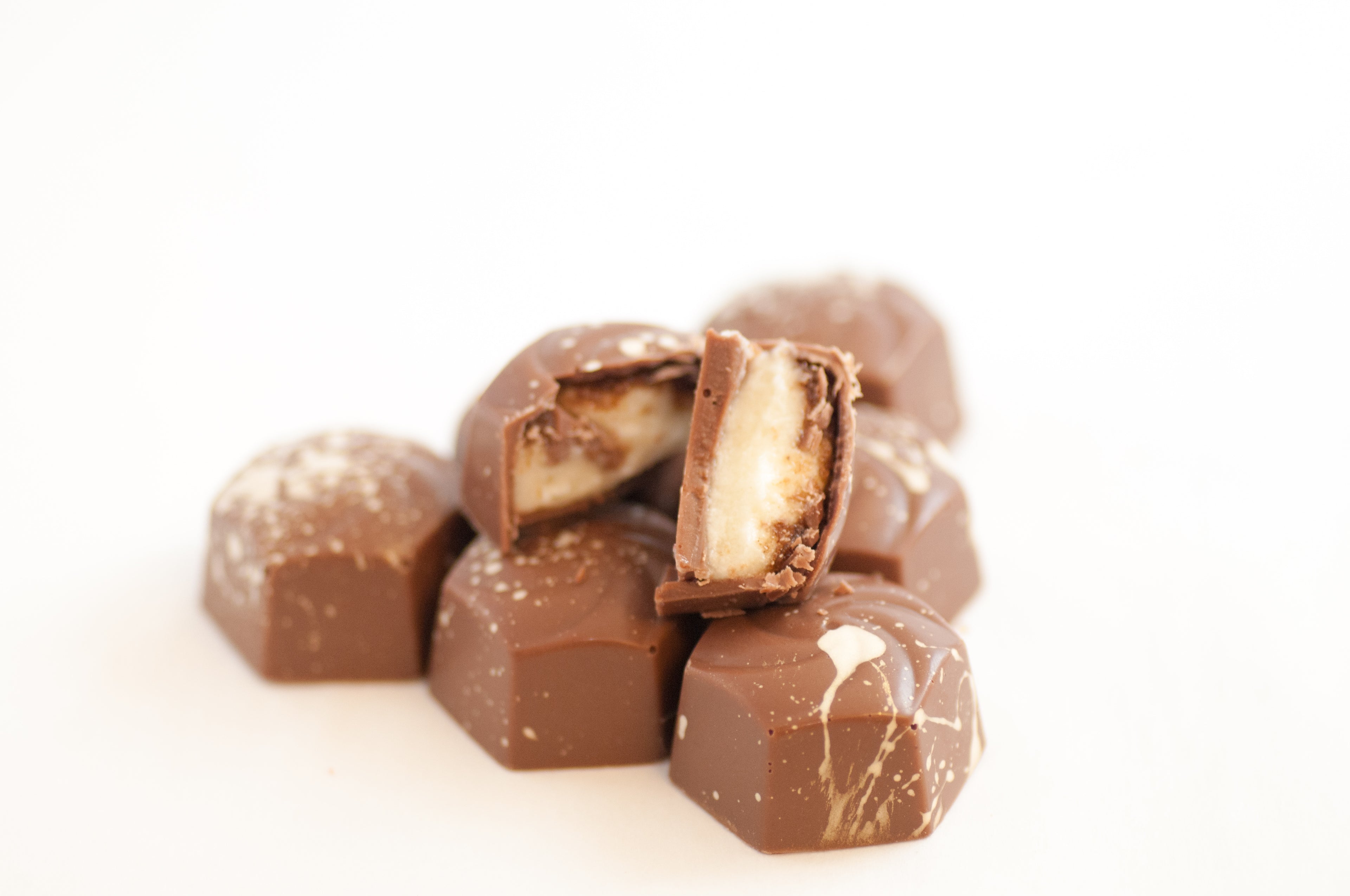 Stack of milk chocolate Cinnamon Roll Bon Bons with one cut open to reveal the layered cinnamon filling.