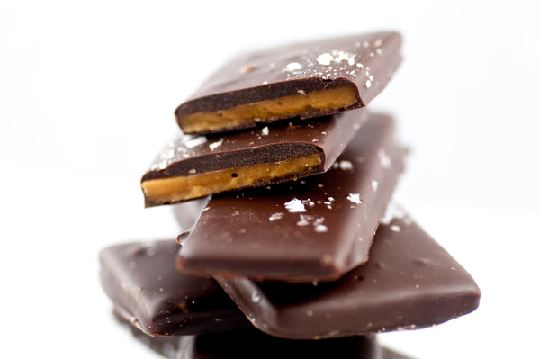Stack of Sea Salt Chocolate Butter Toffee slabs, the buttery toffee visible beneath the dark chocolate-and-sea-salt finish.