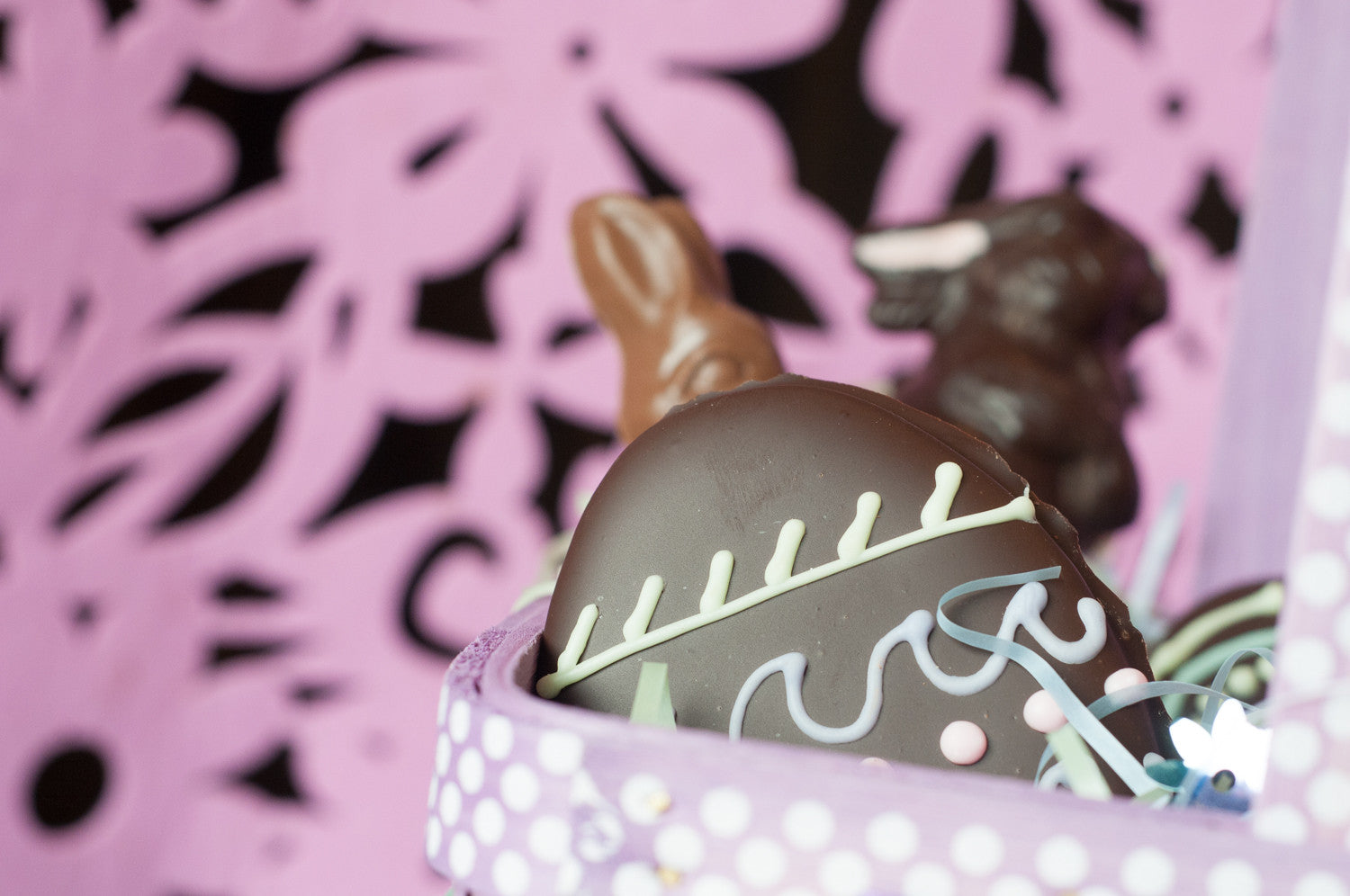 Detail of a piped chocolate Easter egg in the Large Chocolate Easter Basket — white, blue, and yellow decorative piping with pink accents.