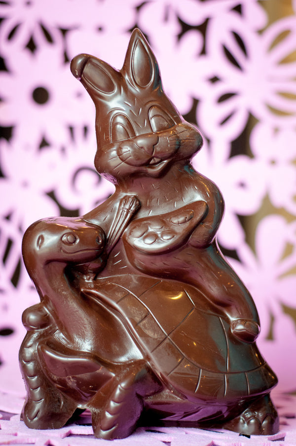 Detailed dark chocolate Easter sculpture of a bunny sitting on a turtle, the bunny holding a carrot.