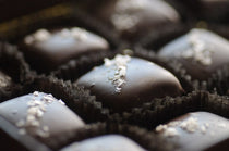 Dark Chocolate Caramels with Sea Salt — close-up of pillow-shaped chocolates topped with flaked sea salt in dark paper cups.