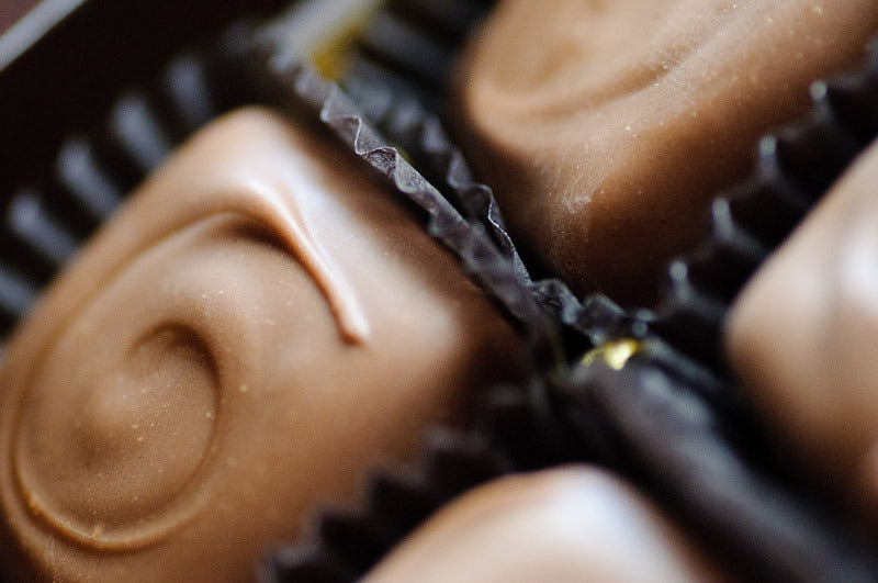 Macro view of milk chocolate-enrobed caramels in dark paper cups, each topped with a piped chocolate swirl. Main image
