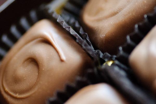 Macro view of milk chocolate-enrobed caramels in dark paper cups, each topped with a piped chocolate swirl.