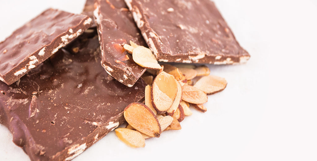 Dark Chocolate Almond Bark — squares of dark chocolate bark with sliced almonds embedded throughout, alongside loose sliced almonds.