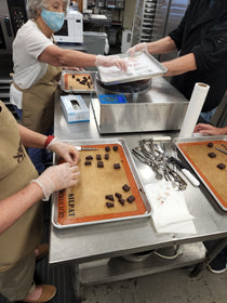 Participants shaping and preparing chocolate truffles during a hands-on workshop at The Secret Chocolatier in Charlotte, NC, with trays and dipping tools in use.