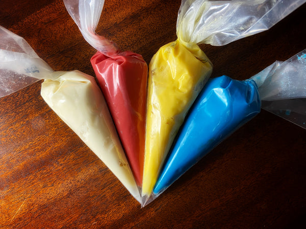Brownie Pop Decorating Kit icing — cream, red, yellow, and blue piping bags ready for decorating.