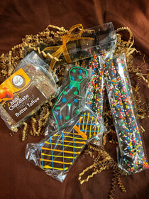 Father's Day gift assortment — Milk Chocolate Hazelnut Butter Toffee, chocolate-covered pretzel sticks with rainbow sprinkles, and chocolate tie cookies on crinkle paper.