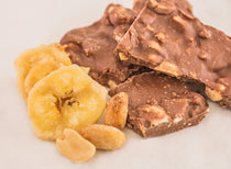 Salty Monkey Milk Chocolate Bark — milk chocolate pieces studded with peanuts, shown with banana chips and whole peanuts alongside.